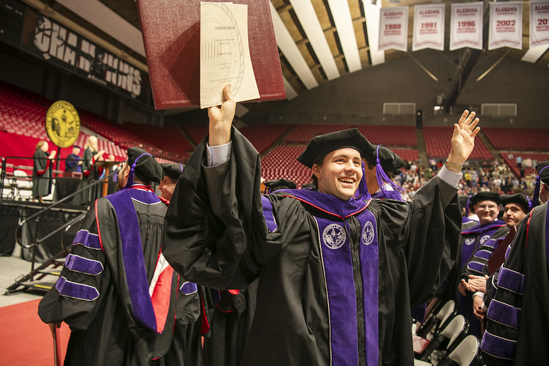 Alabama Law student celebrates with diploma in the air after graduation.