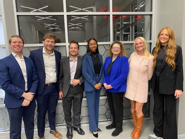 a group of seven people standing in a line dressed in business-professional attire