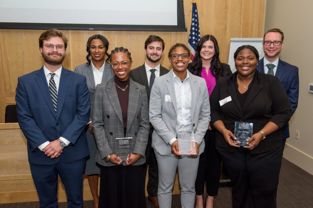 a group of eight law students in business professional attire. the three students in the front are holding plaques.