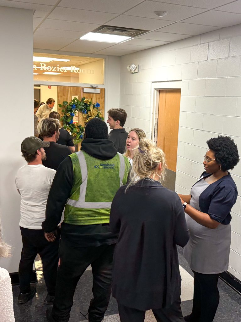 a group of people stands in hallway in line to enter a room.