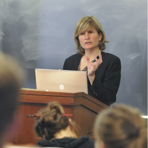 Professor Helen Norton lecturing at the front of a classroom with a laptop open in front of her