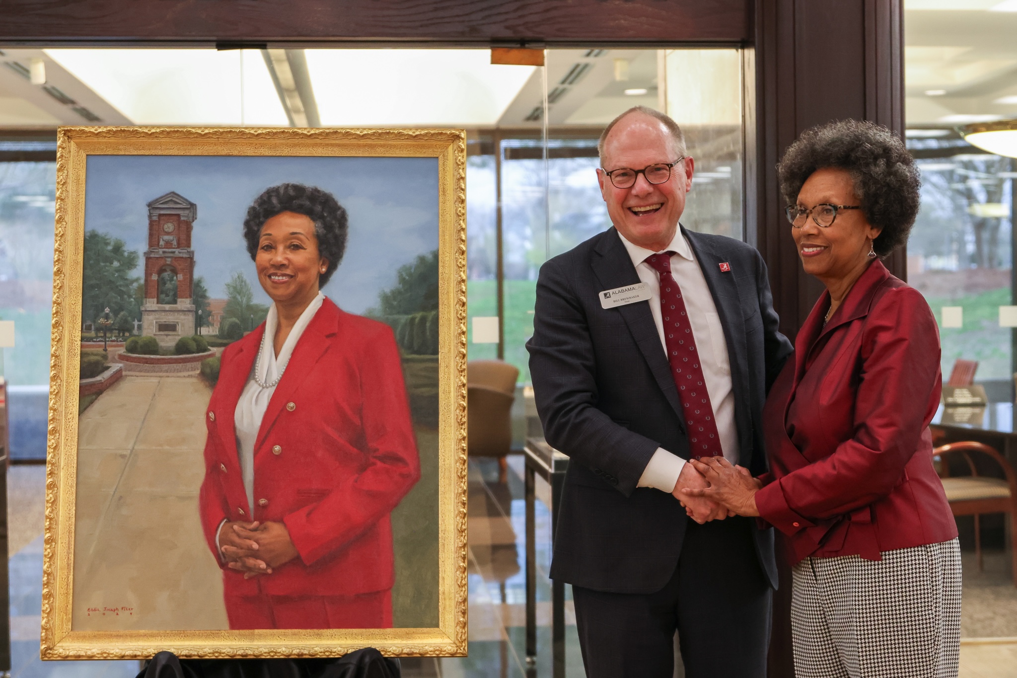 A man shakes hands with a woman while standing next to a commemorative portrait of the woman.
